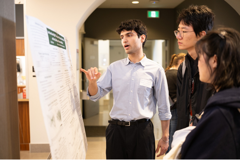 A student presenting an honours thesis poster to two classmates