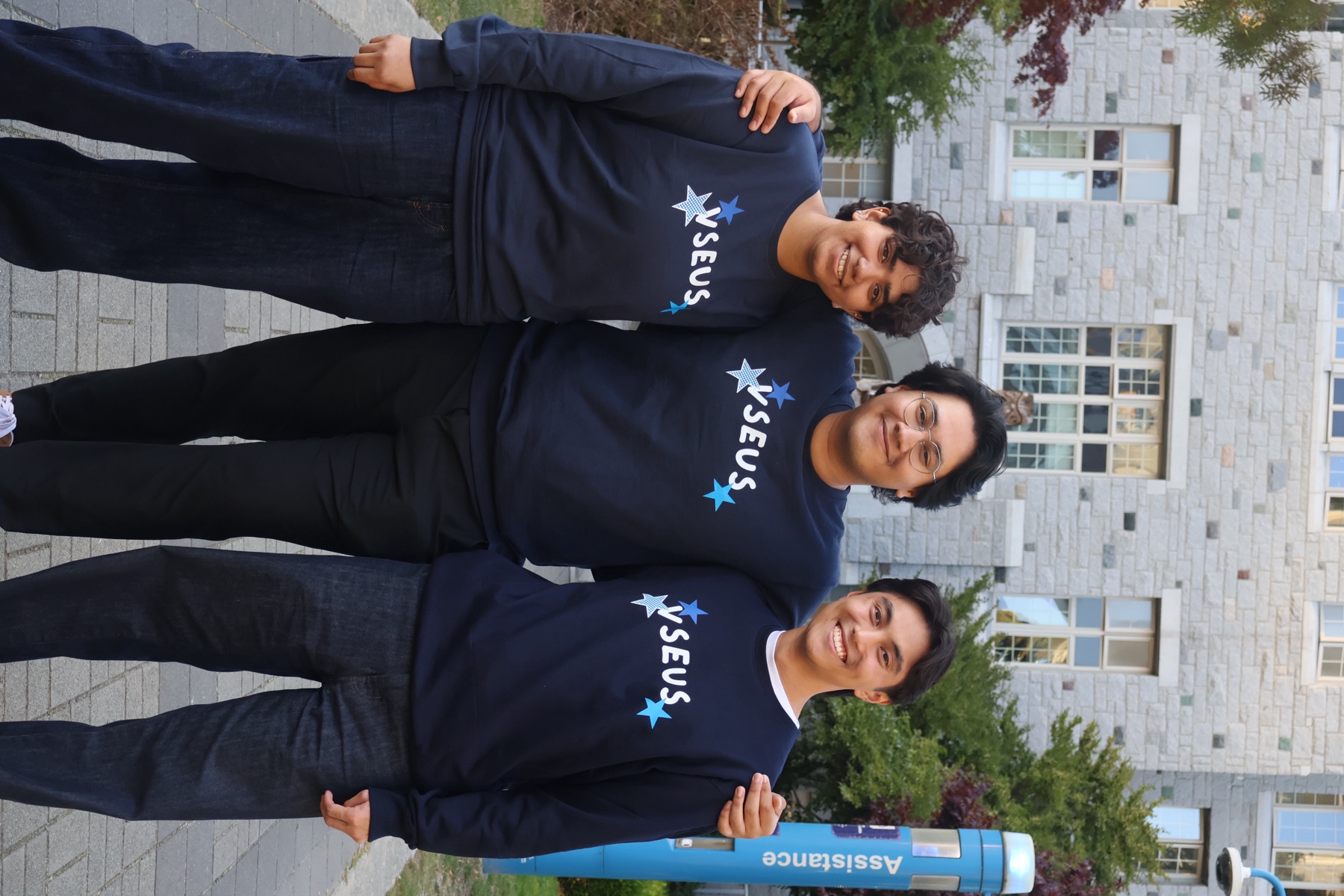 Three students arm in arm outside a stone campus building in navy VSEUS sweaters