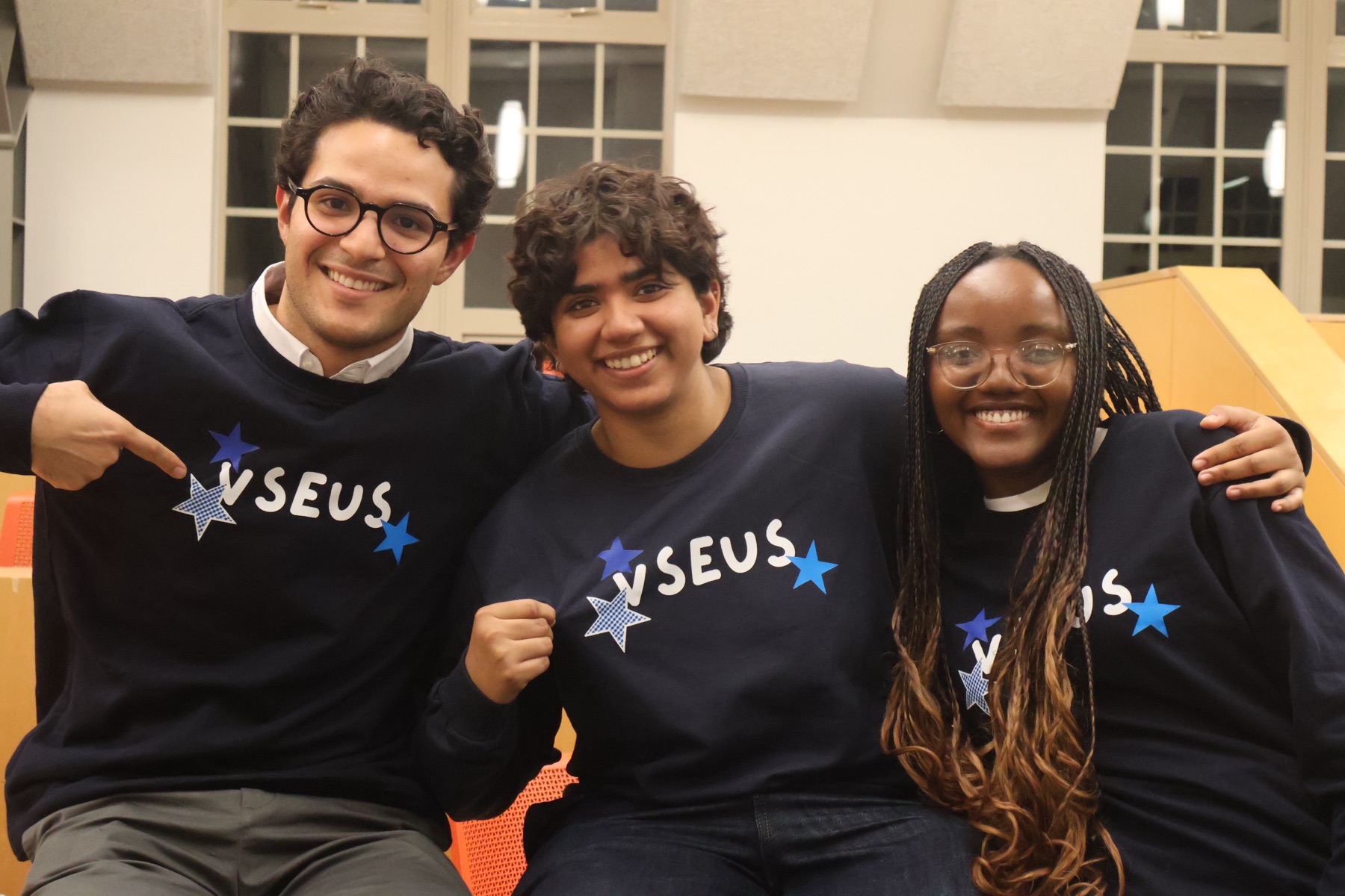 Three students smiling in navy VSEUS sweaters with the starred VSEUS print