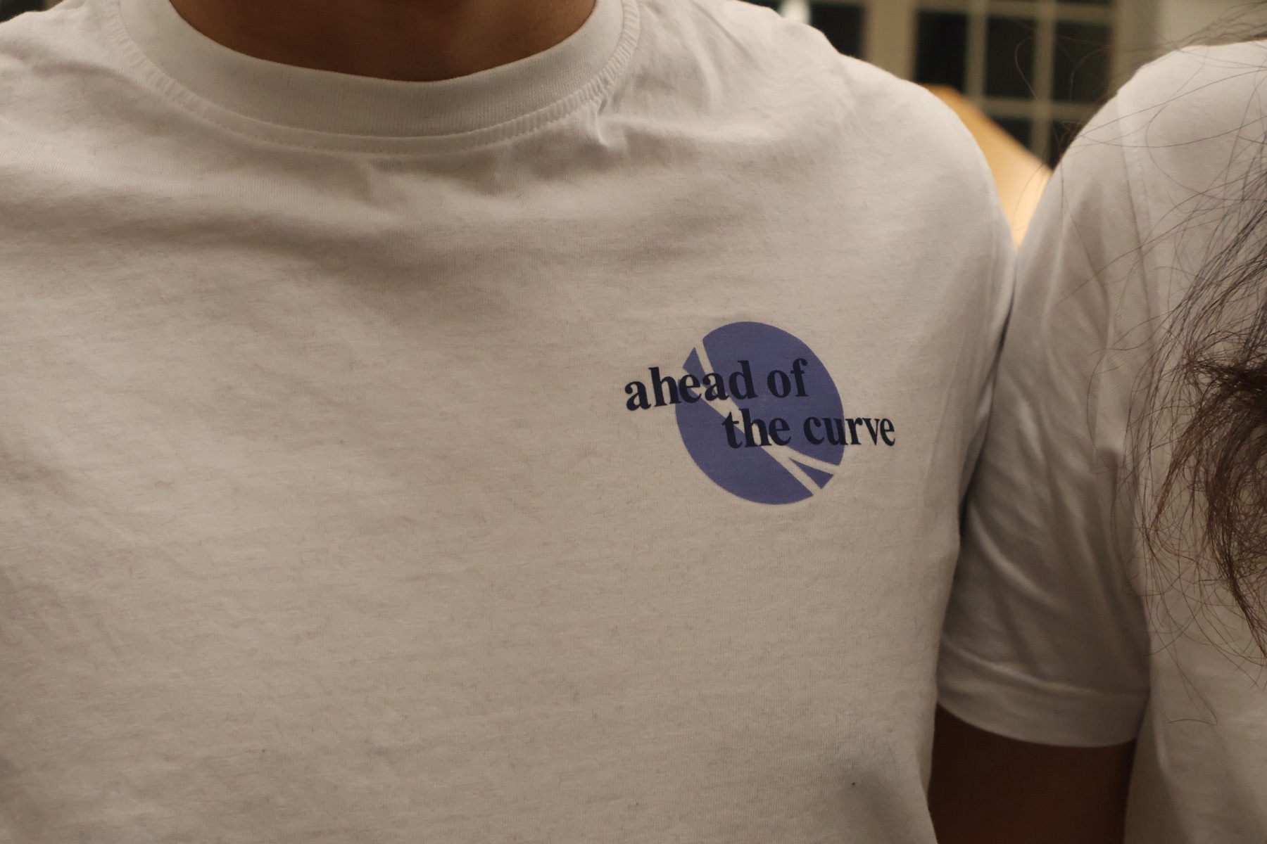 Close-up of the "ahead of the curve" chest print on a white VSEUS tee
