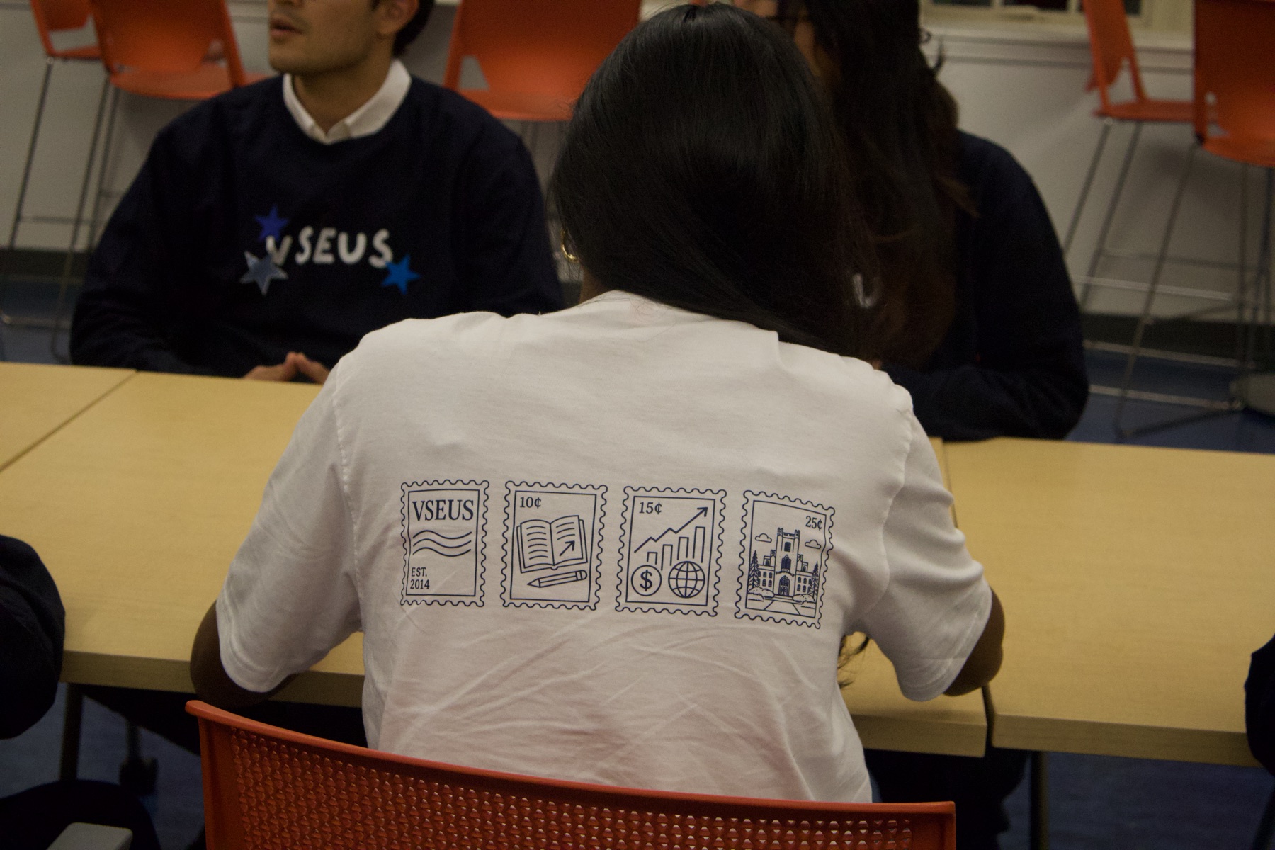 Back of a white VSEUS tee printed with a row of four stamp illustrations